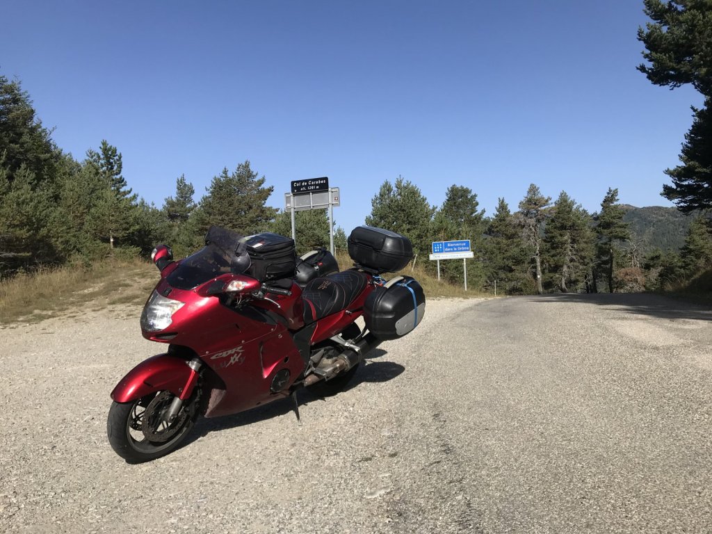 Rotes Reisemotorrad mit Koffern auf einem Schotterplatz an einer Passhöhe