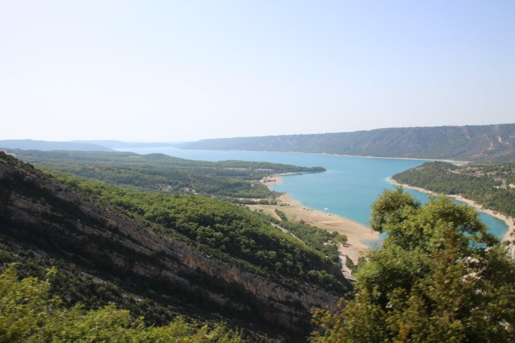 Türkisfarbener See zwischen bewaldeten Hängen und einem Sandstrand