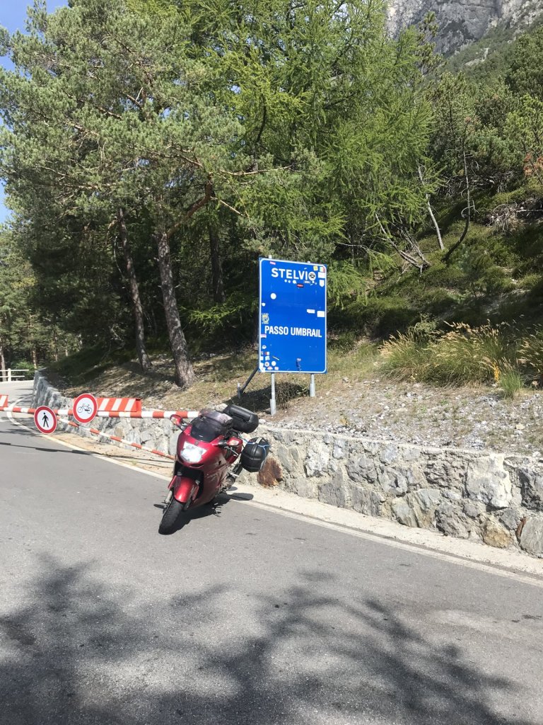 Rotes Motorrad an der Straße am Passo Umbrail mit Schild Stelvio
