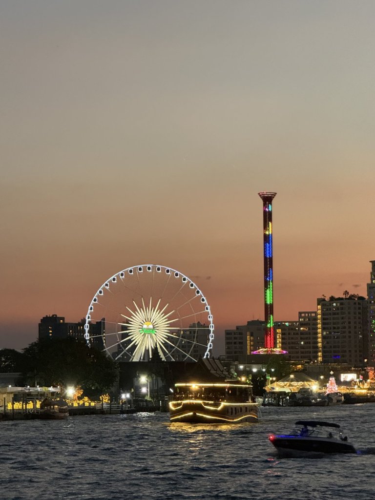 Riesenrad und beleuchteter Turm am Flussufer bei Sonnenuntergang