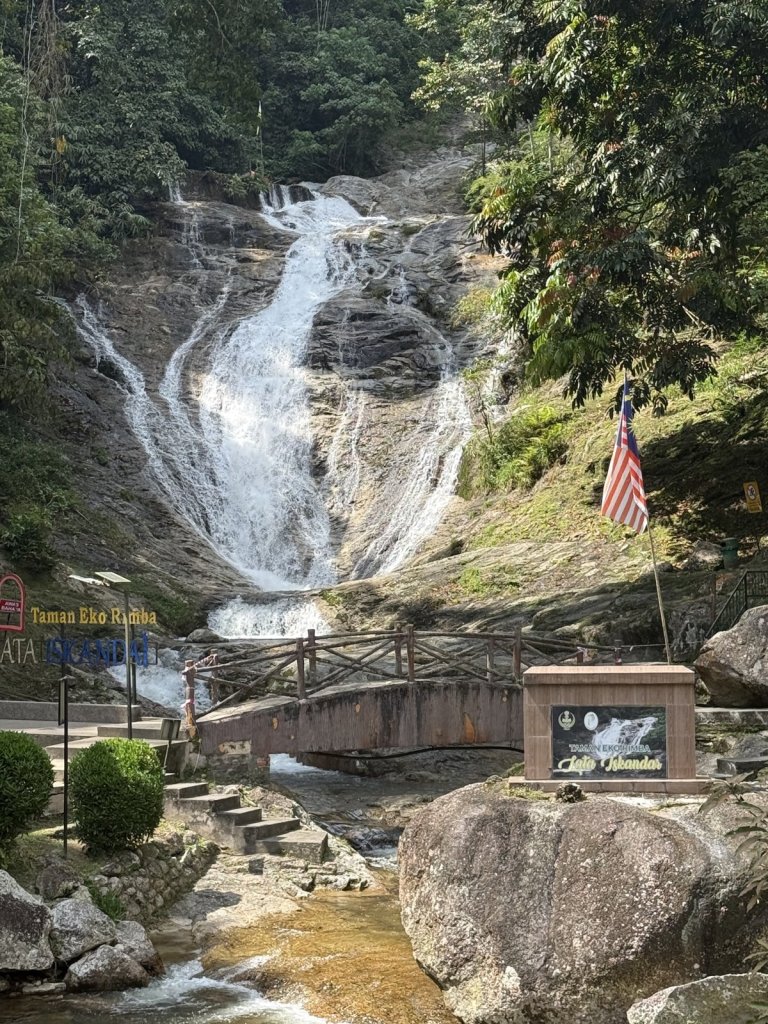 Wasserfall über Felsen mit einer Brücke und der Flagge Malaysias