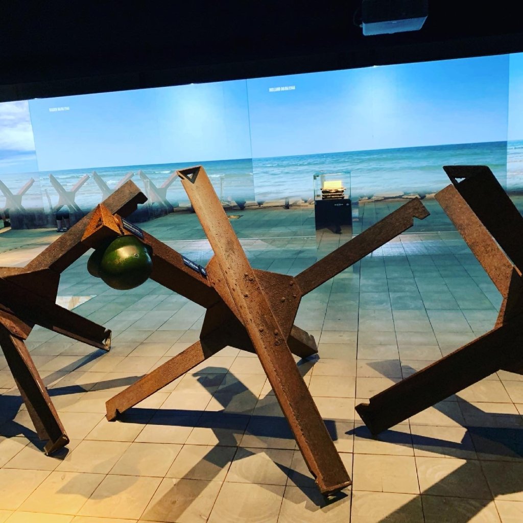 Rostige Panzersperren in einer Ausstellung vor einer Strandkulisse