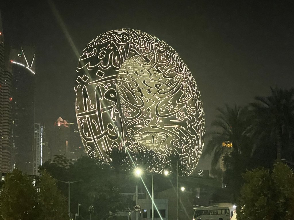 Ovales Gebäude mit arabischer Kalligrafie, nachts beleuchtet