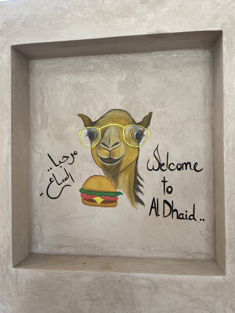 Wandbild eines Kamels mit Brille und Burger und dem Schriftzug Welcome to Al Dhaid