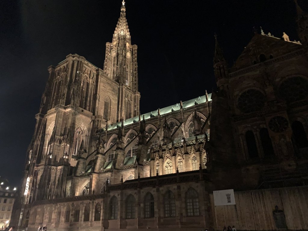 Beleuchtetes Straßburger Münster mit Turm hinter Dächern