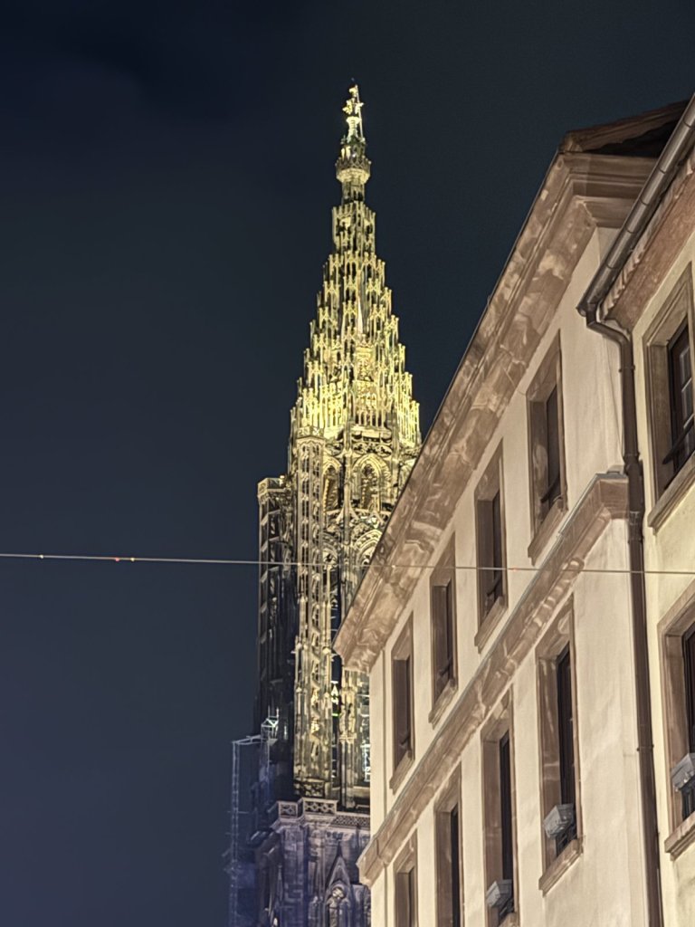 Beleuchteter Turm des Straßburger Münsters neben einem Haus