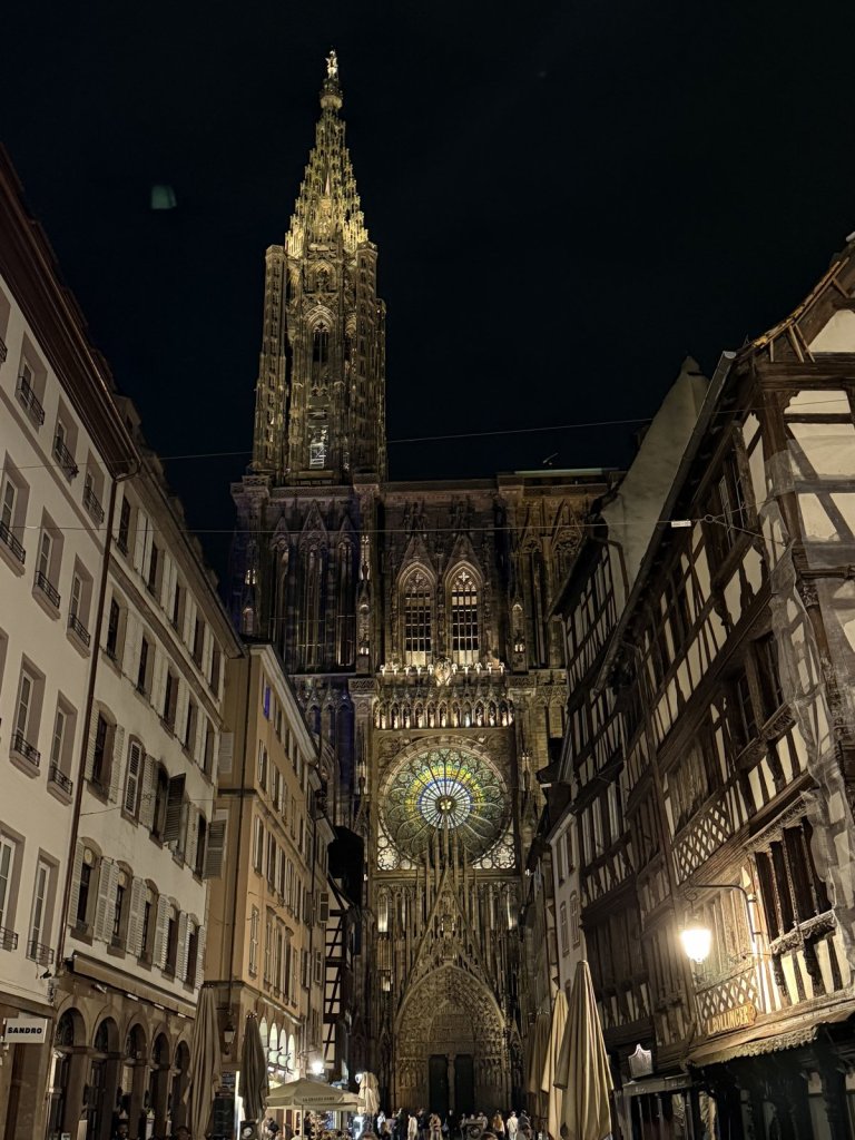 Blick durch eine Gasse mit Fachwerkhäusern auf die beleuchtete Fassade des Straßburger Münsters