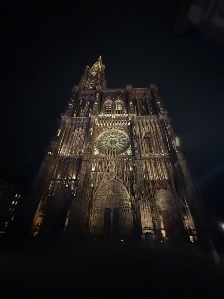 Beleuchtete Westfassade des Straßburger Münsters mit Rosette in der Nacht