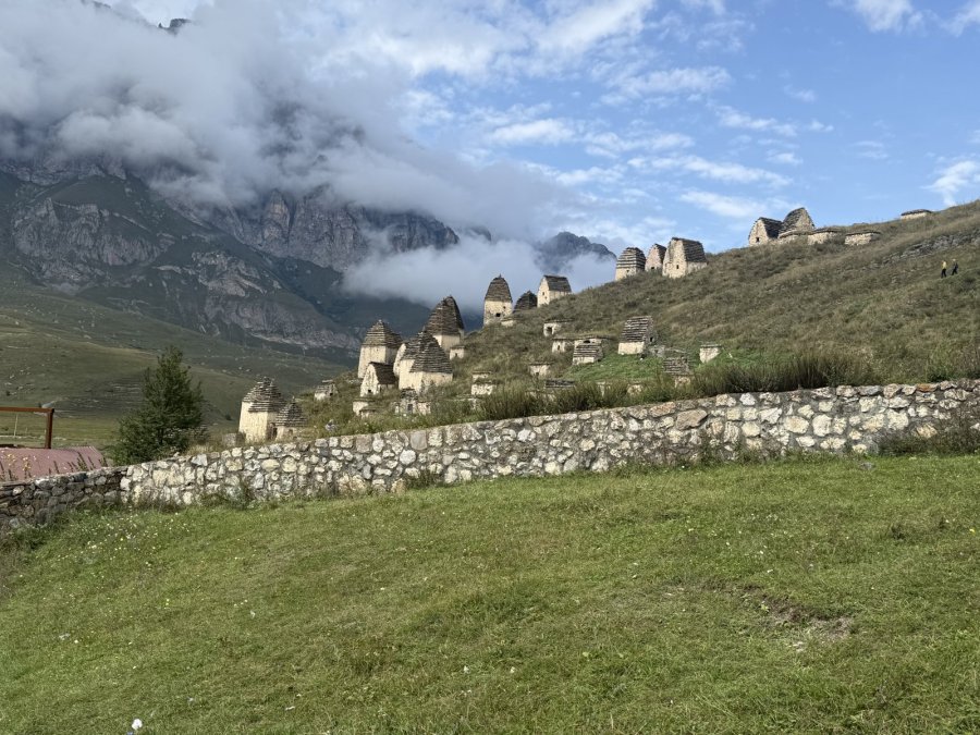Kleine Steinhäuser der Totenstadt Dargavs auf einem Hang unter Wolken in Nordossetien