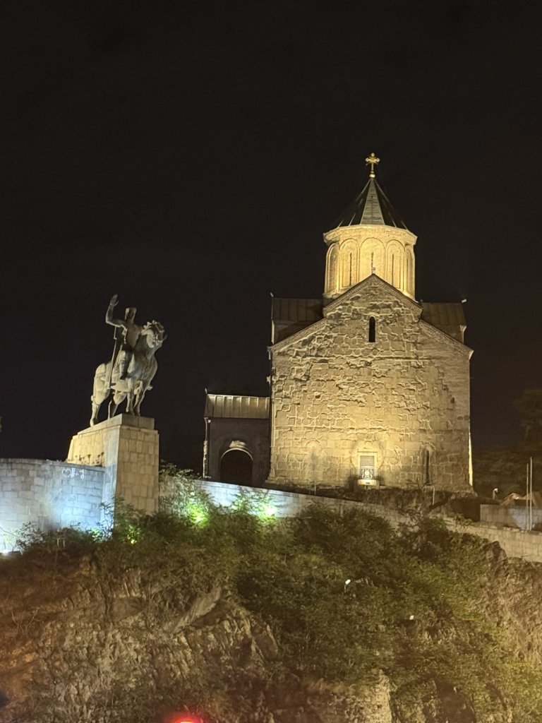 Beleuchtete Metechi-Kirche mit dem Reiterstandbild auf einem Felssporn in Tiflis