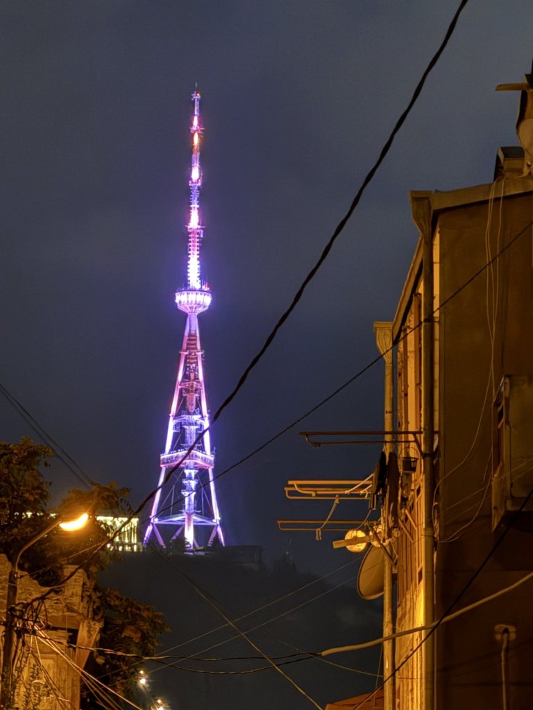 Beleuchteter Fernsehturm von Tiflis in der Nacht zwischen Häusern
