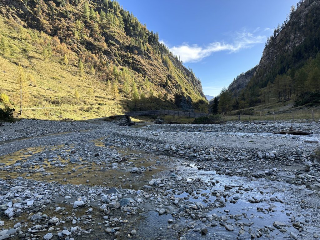 Breites Kiesbett eines Gebirgsbachs zwischen herbstlichen Berghängen