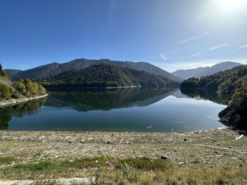 Spiegelnder Stausee mit bewaldeten Bergen