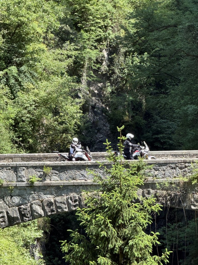 Zwei Motorräder auf einer Steinbrücke über einer bewaldeten Schlucht