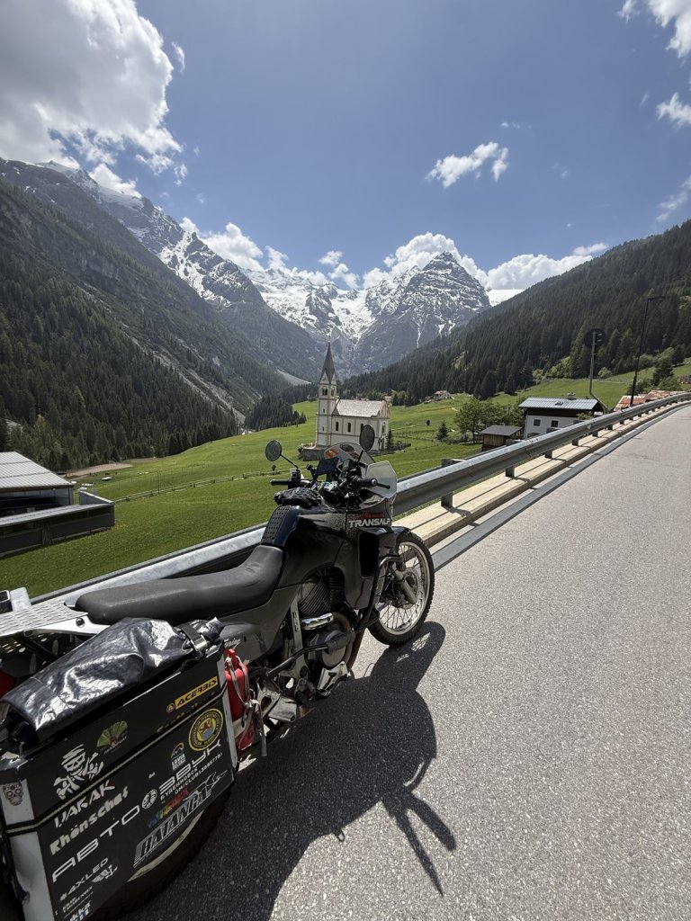 Motorrad auf der Straße im Tal, dahinter Gletscher und Kapelle