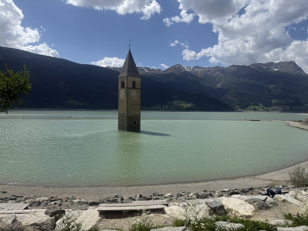 Kirchturm ragt aus dem Reschensee, dahinter Berge
