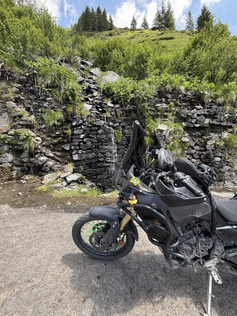 Schwarzes Reisemotorrad vor einer Trockenmauer und Wiesen am Wasserfall