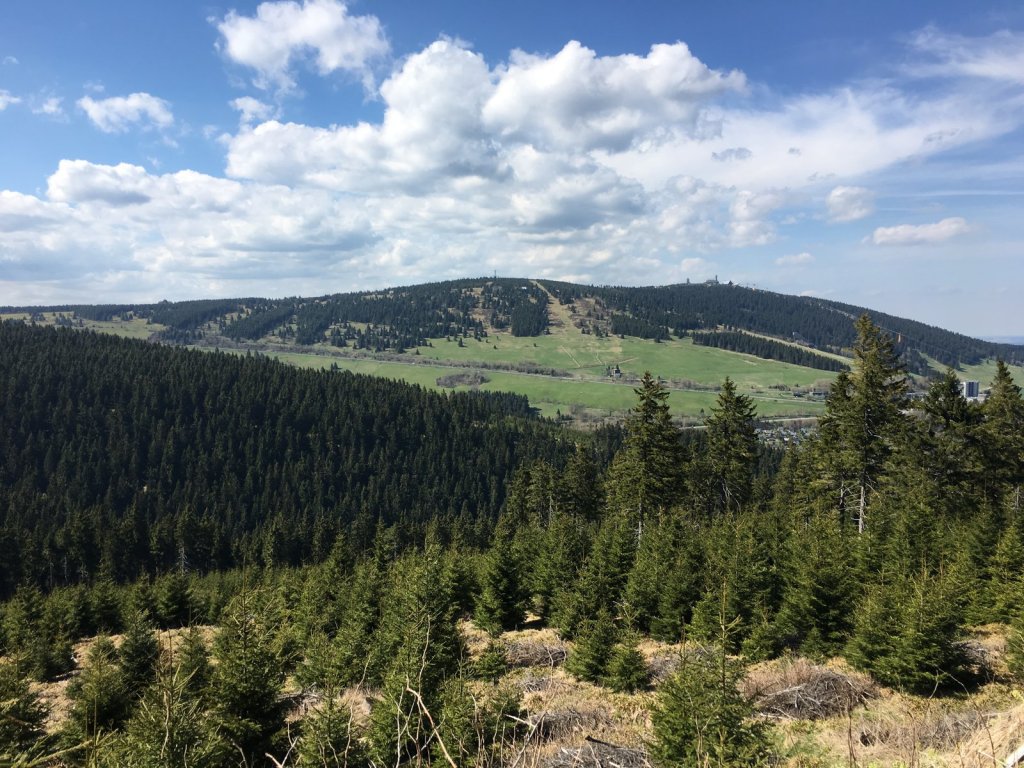 Bewaldete Hügel und ein Gipfel mit Sendeturm unter Wolken im Erzgebirge