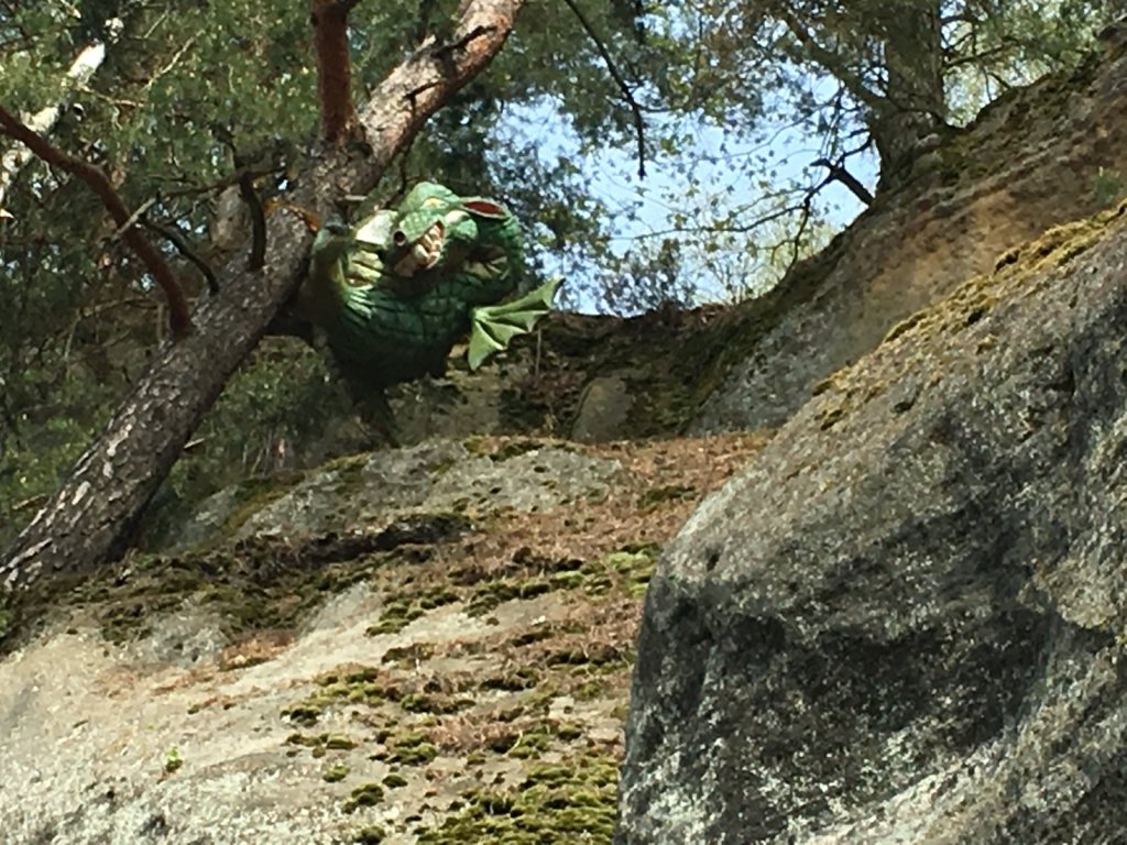 Figur eines grünen Drachen auf einem Sandsteinfelsen unter Kiefern