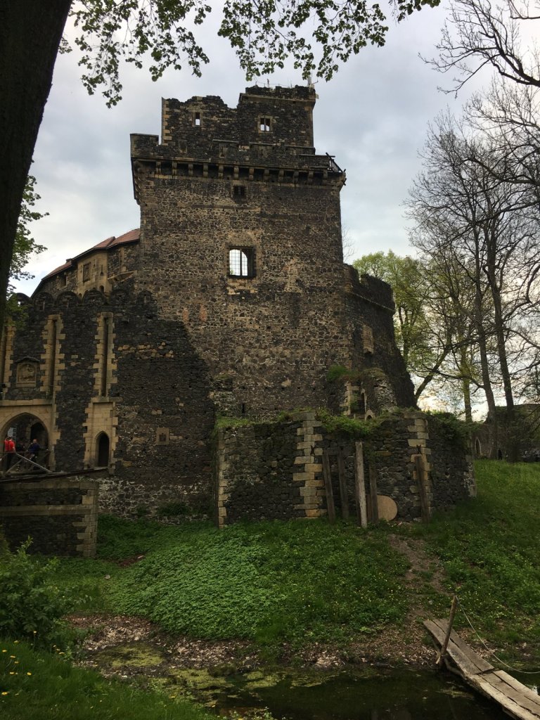 Turm einer Burgruine aus dunklem Stein mit Wassergraben im Vordergrund
