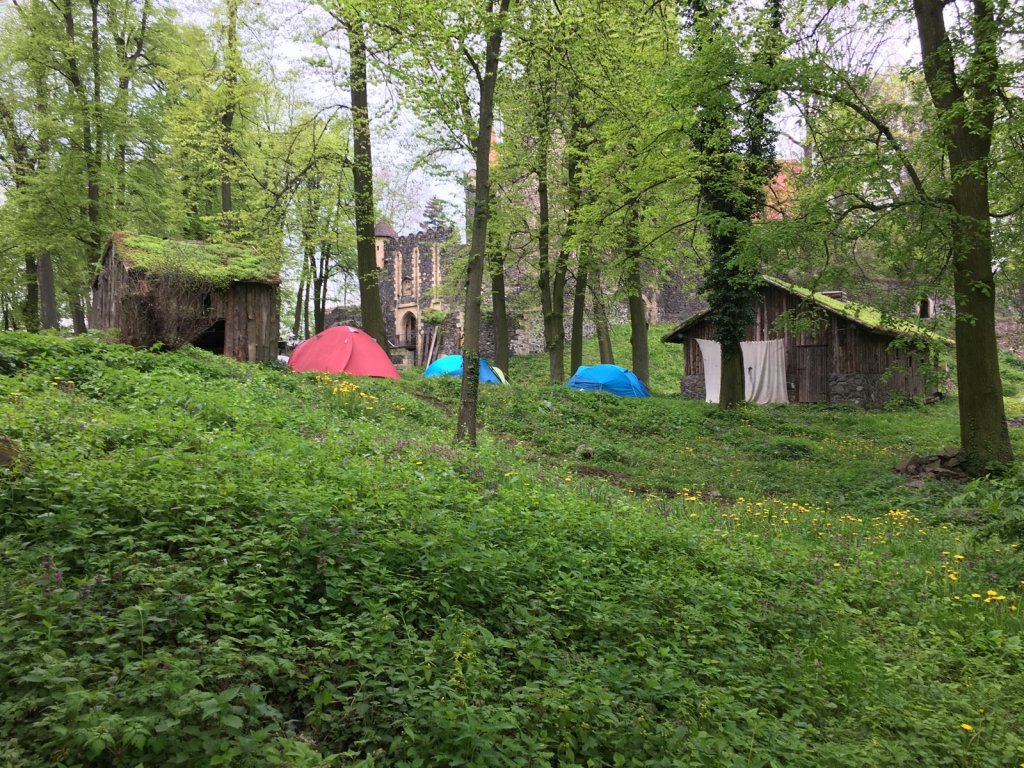 Grüner Burggraben mit Zelten und Holzhütten zwischen Bäumen