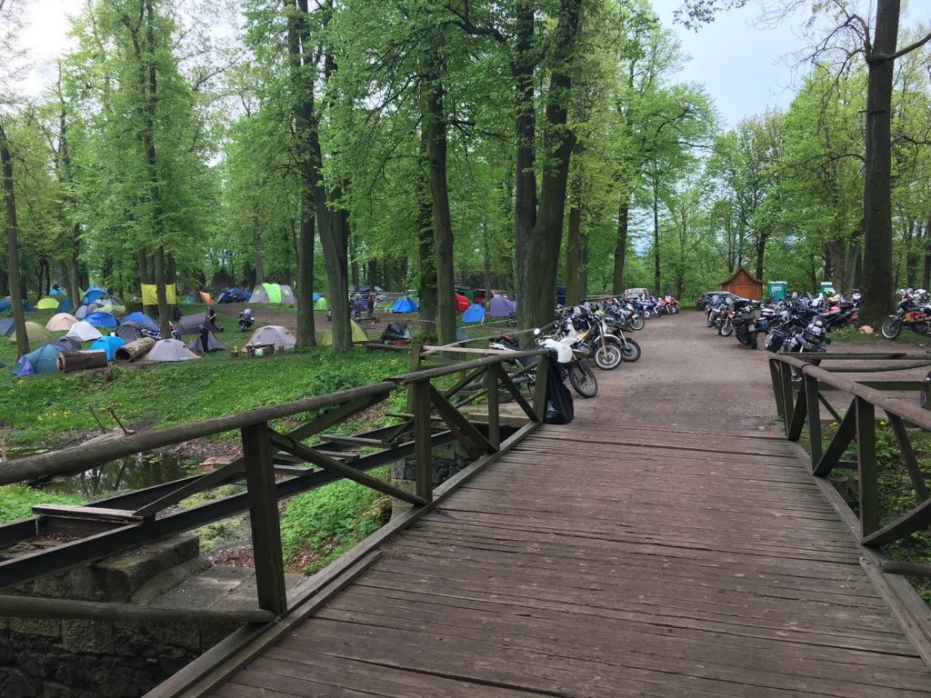 Holzsteg durch den Wald zum Zeltplatz, links Zelte und rechts parkende Motorräder