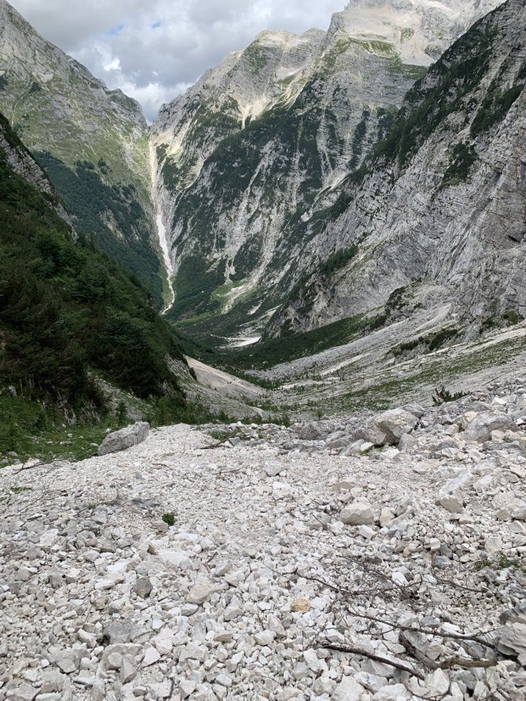 Geröllfeld in einem Hochtal mit steilen Felswänden und einem Wasserfall