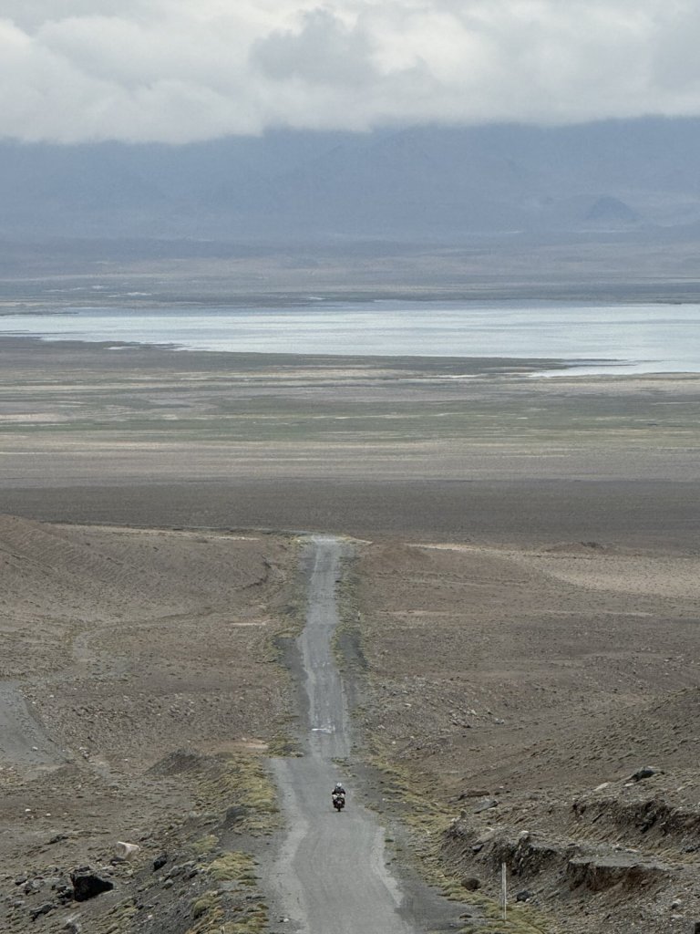 Lange Piste hinab zum Karakul-See, ein Motorrad ganz klein auf der Straße