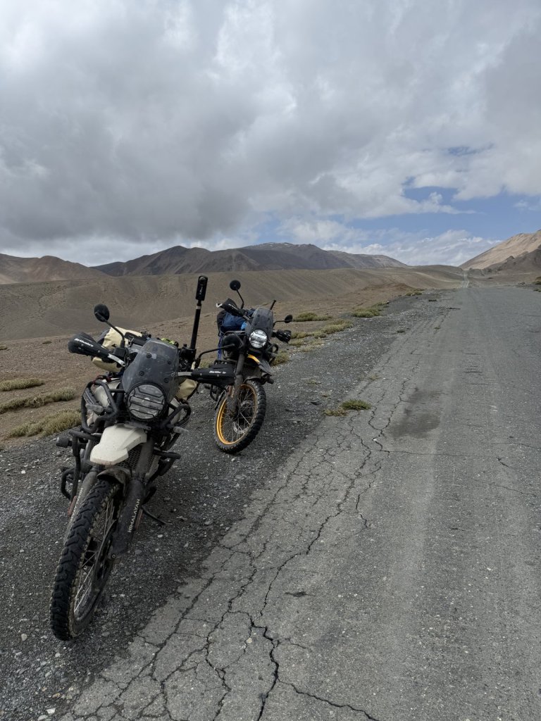 Zwei Leihmotorräder auf rissigem Asphalt, dahinter Berge und Wolken