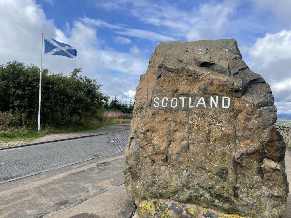 Grenzstein mit der Aufschrift Scotland und der schottischen Flagge an der Straße