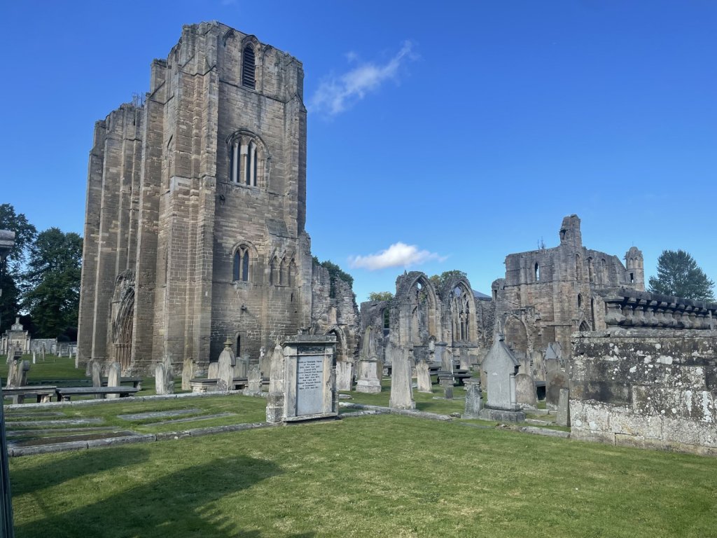 Ruine der Elgin Cathedral mit Türmen und Friedhof unter blauem Himmel
