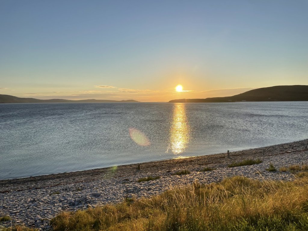 Sonne geht über einem Loch bei Ullapool unter, davor ein Kiesstrand