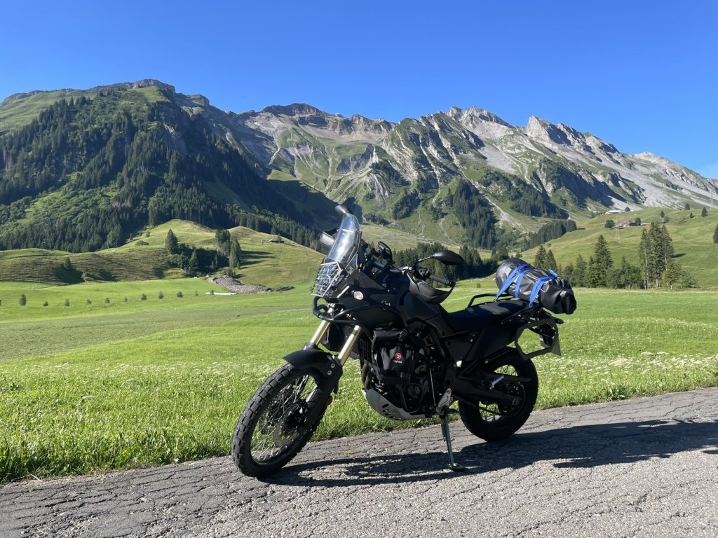 Motorrad mit Gepäck auf einer Straße vor grünen Almwiesen und Bergen