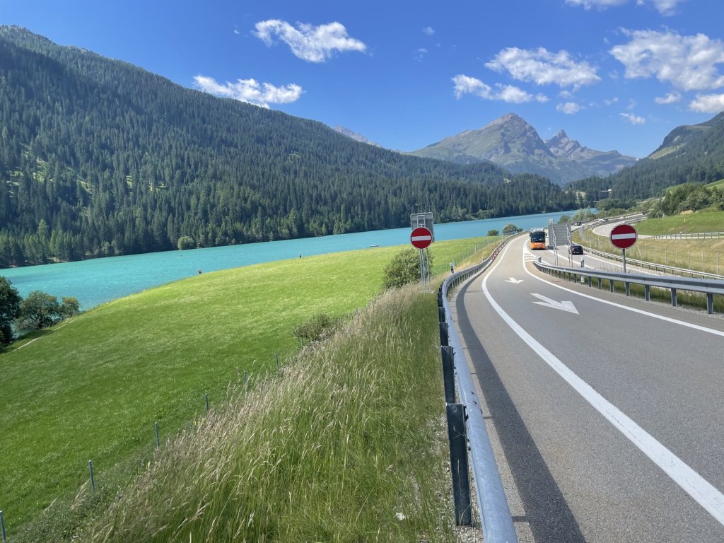Türkisfarbener Stausee neben einer Straße zwischen Bergen und Wald