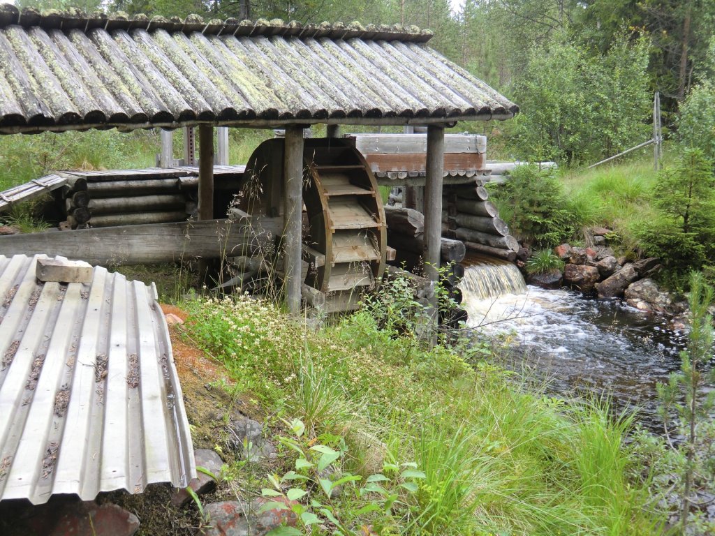 Hölzernes Wasserrad unter einem Schindeldach an einem Bach