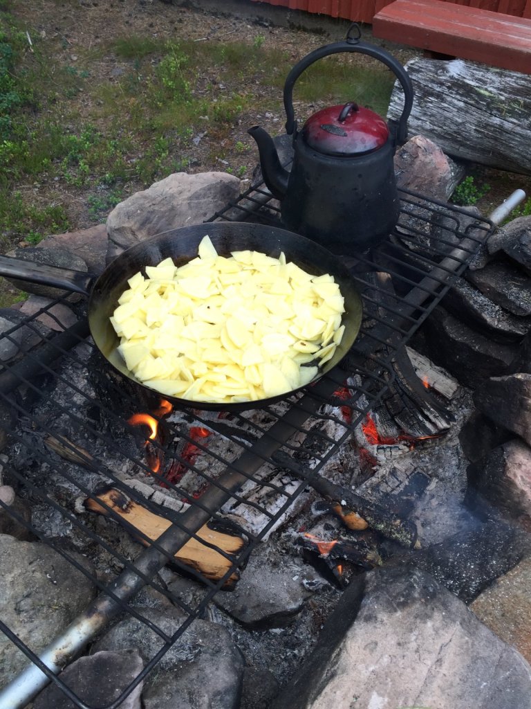 Pfanne mit Bratkartoffeln und Wasserkessel über offenem Feuer