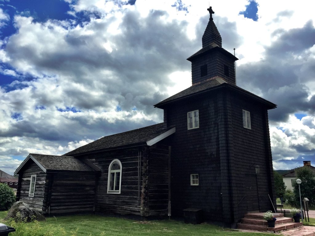 Schwarze Holzkirche mit Glockenturm unter Wolkenhimmel
