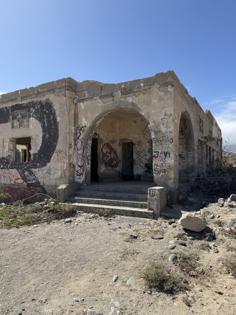 Verfallenes Gebäude mit Bogengang und Graffiti auf kargem Küstenland