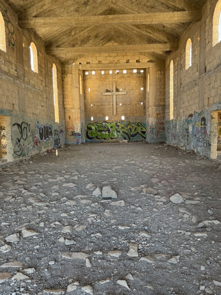 Innenraum einer verfallenen Kirche mit Kreuz an der Stirnwand und Graffiti