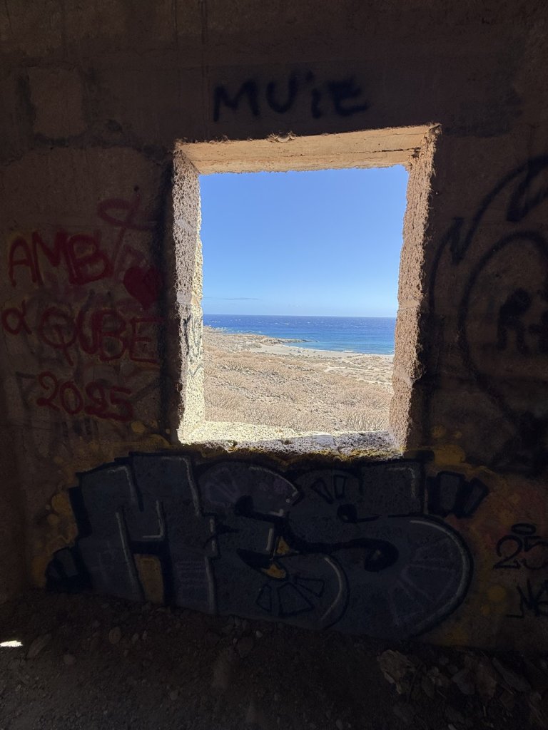 Blick durch ein Fenster einer Ruine auf Strand und Meer