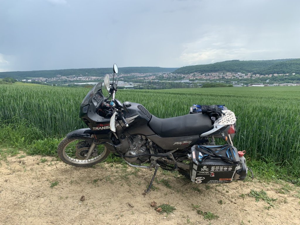 Honda Transalp mit Gepäck am Rand eines Weizenfelds, im Hintergrund ein Tal