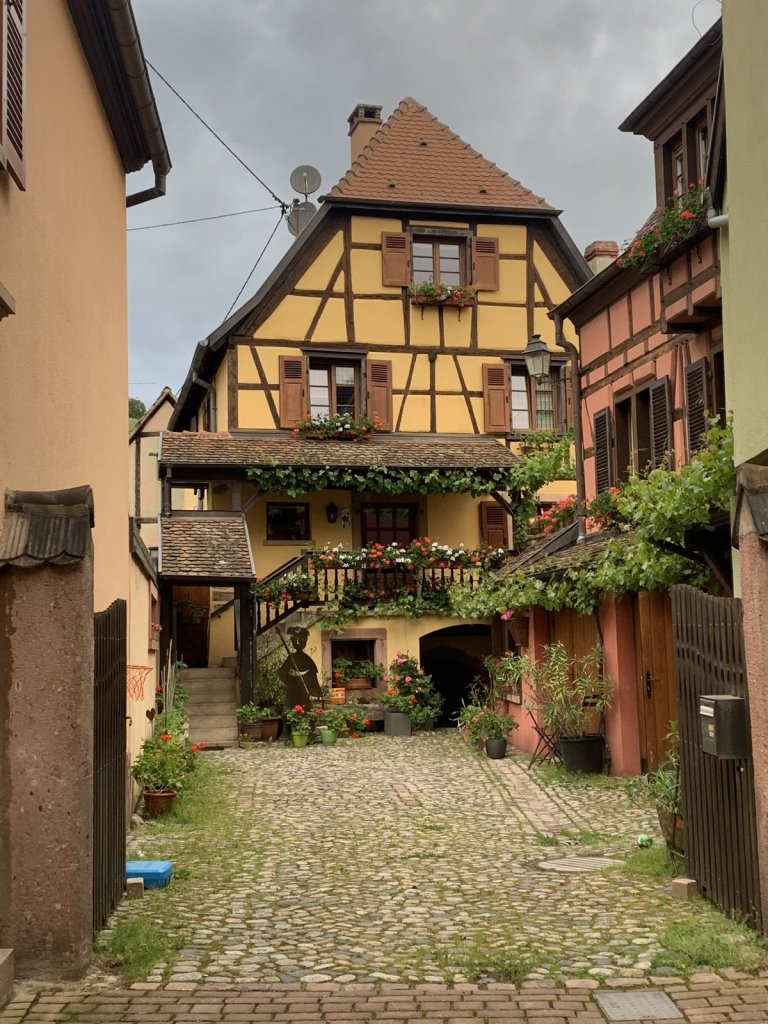 Gelbes Fachwerkhaus mit Blumen in einem gepflasterten Hof