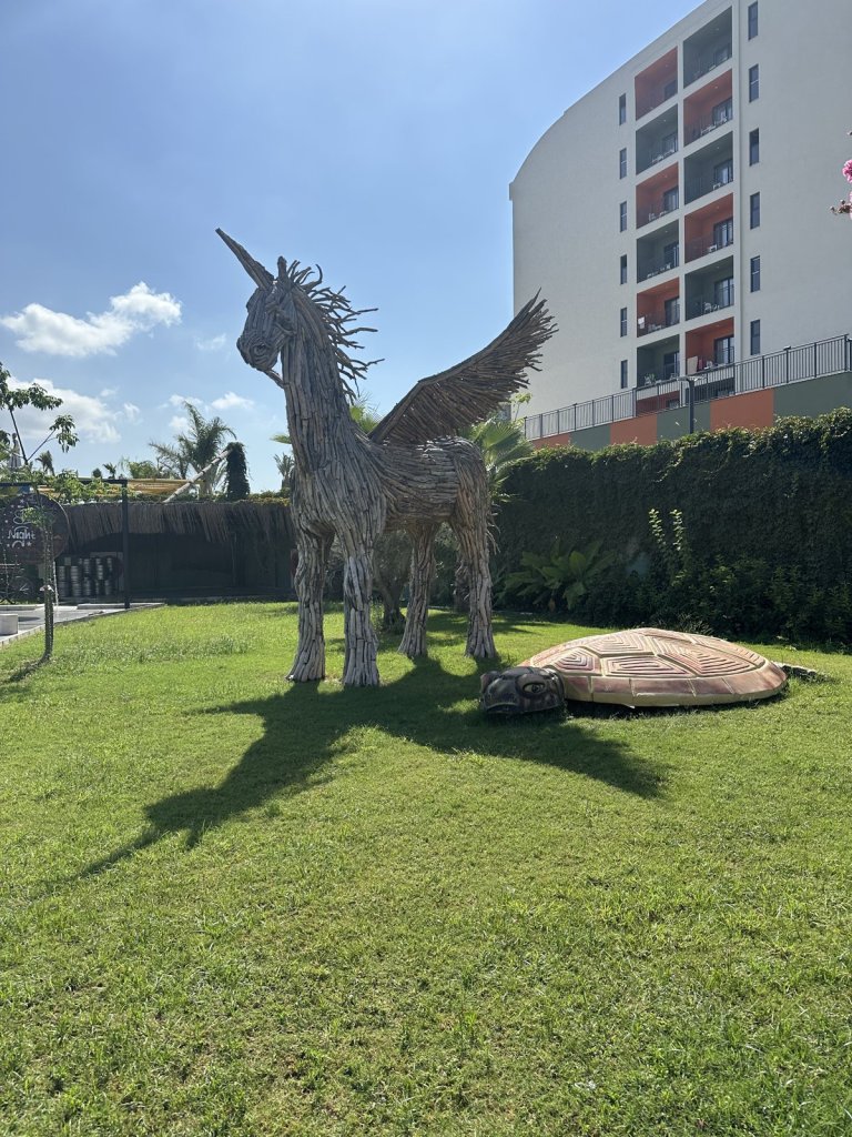 Skulptur eines geflügelten Pferdes aus Treibholz auf einer Wiese vor einem Hotel